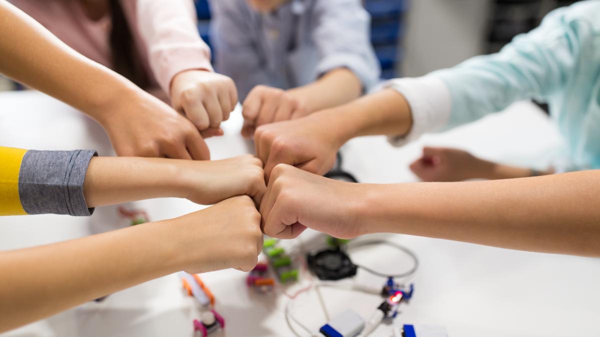 Close-up photo of children bumping fists over top of a tabletop in a classroom