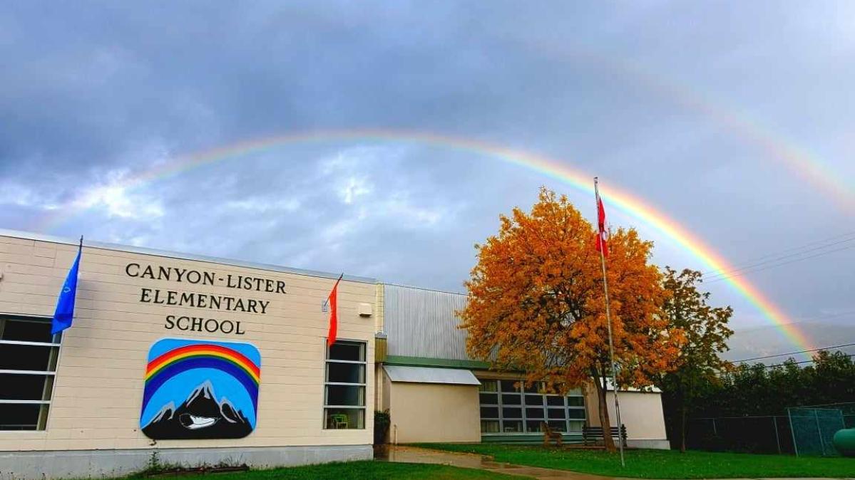 Elementary school with rainbow sign and double rainbow against billowy cloud-covered sky in background