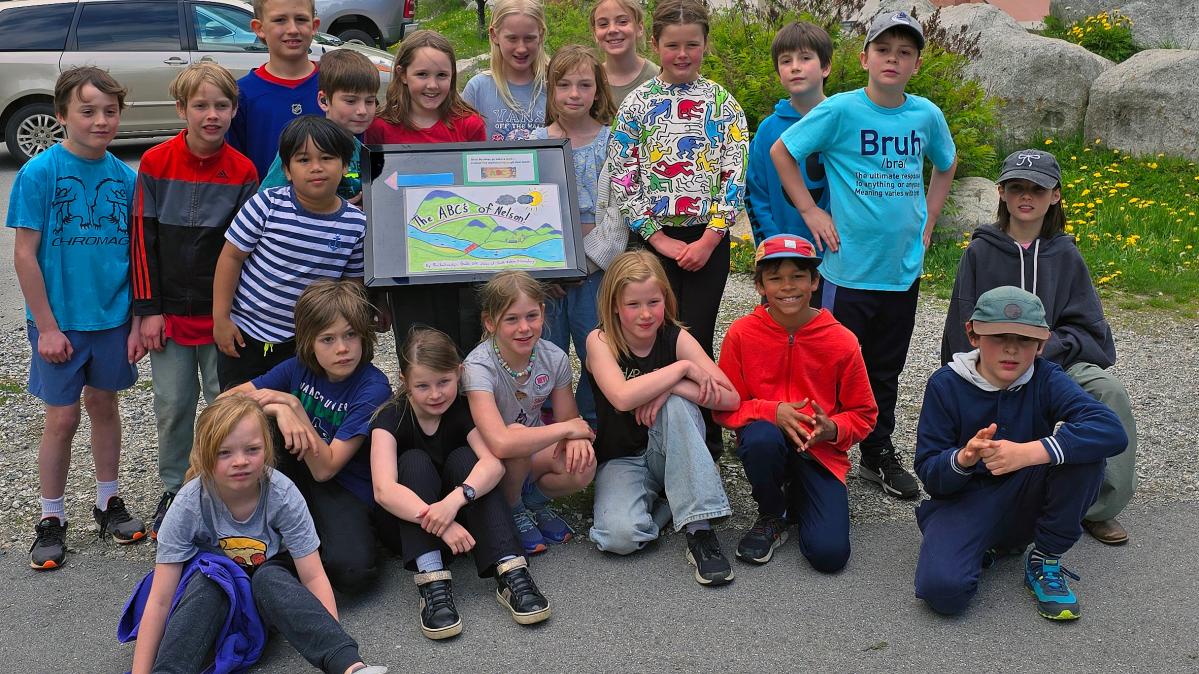 A group of elementary school students pose in front of a display board in a park