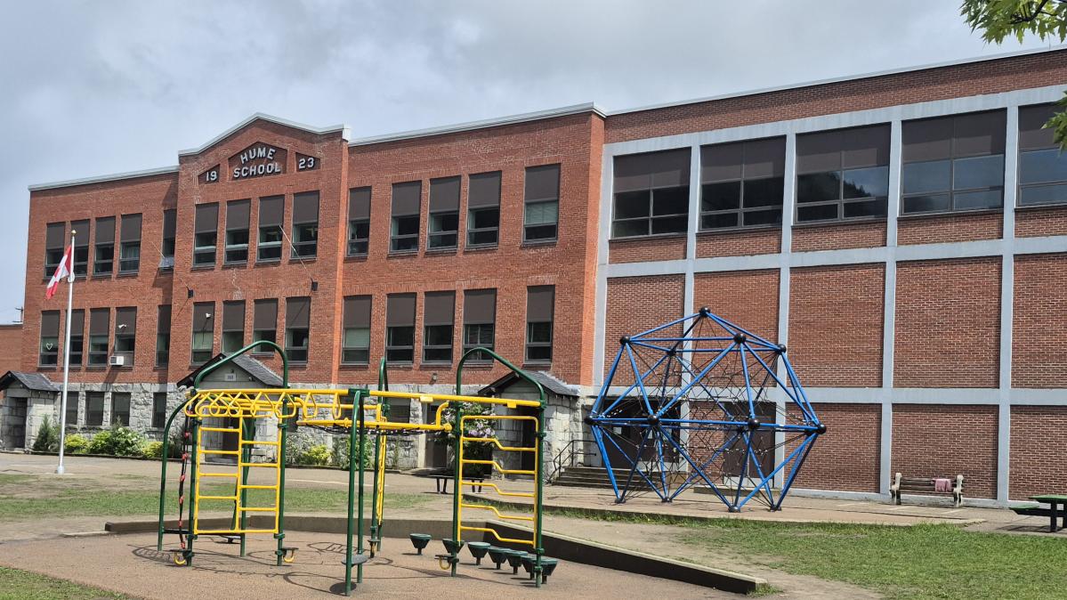 A rectangular brick school building with a playground in front.