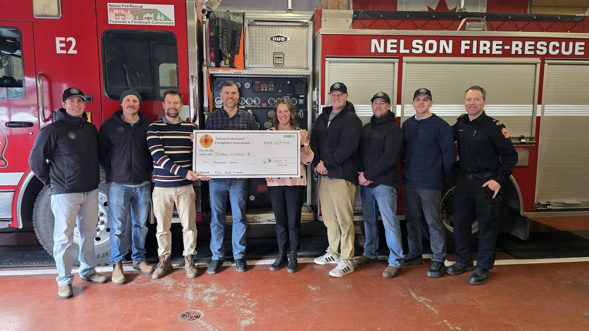 A group of people stand in front of a fire truck holding a large, cardboard cheque