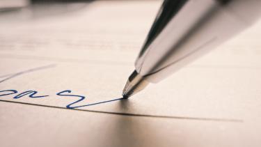 Close-up of blue, ballpoint pen tip at tail end of signature on document