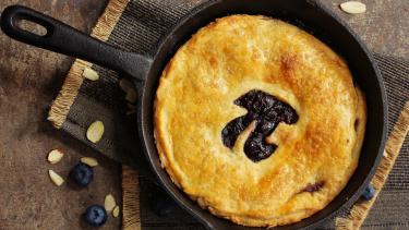 Pie in a cast iron pan on top of a rustic placement on wooden table. Pastry shows cutout of the Greek letter and mathematical symbol Pi.