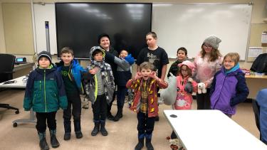 Day of Learning Elementary school children standing in a classroom with winter jackets, boots and toques on, making faces, smiling, watching.