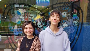 Two smiling female students standing in front of a shop window