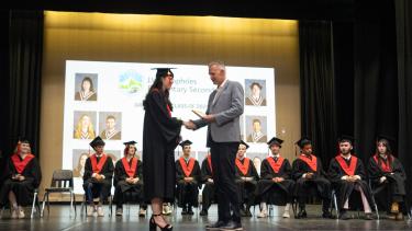 Madyson Isaak receives her diploma from Director Ben Eaton at JVH graduation. Young woman in cap and gown shakes hand of man in grey suit