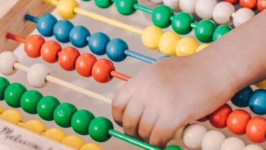 Child's hand moving coloured wooden beads on an abacus