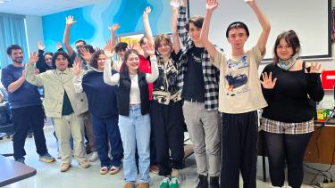 A group of young people and their teachers with hands raised in celebration in a school classroom