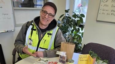Shark Bus Driver Richard Zimmerman A man in a ball cap, glasses and a flourescent green vest sits at a table covered in hand-drawn cards and messages.