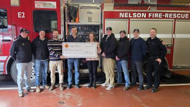 A group of people stand in front of a fire truck holding a large, cardboard cheque