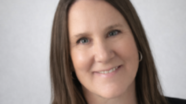 A woman with shoulder-length brown hair wearing a black blazer and white button-up shirt.