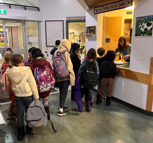 Elementary school children lined up at school kitchen service window to get hot breakfast