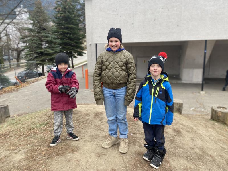 Three elementary students standing on a mound of dirt in front of their school