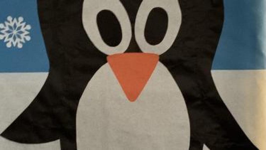 Textile penguin cutout on blue and white background with white snowflake showing.