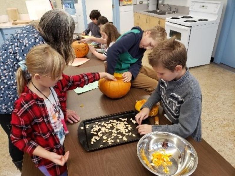 Children gathered around a table sorting pumpkin seeds from a bowl to a cookie sheet for drying.