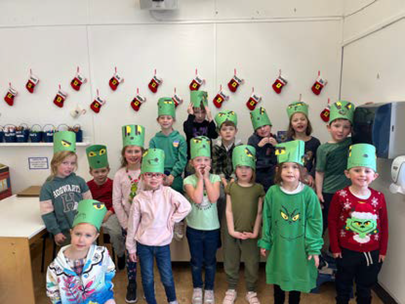 Primary children in green hats looking at camera in classroom decorated for Grinch Bingo