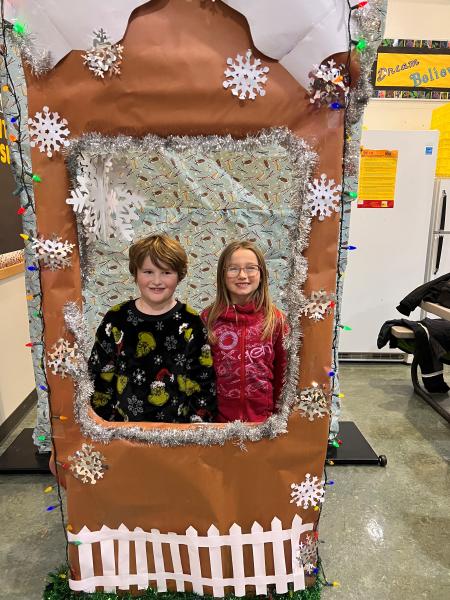 A smiling boy and girl inside a photo booth framed by snowflakes on a brown background