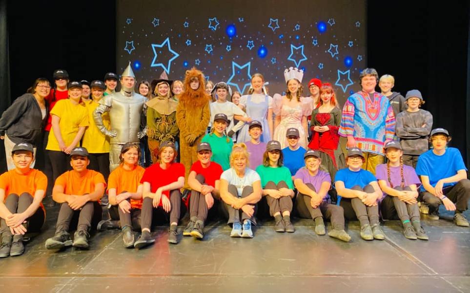 Students in colourful t-shirts sitting and standing as part of the cast of a school production of "OZ"