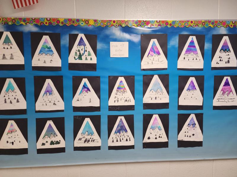 A series of mountain-shaped white triangles on top of black rectangles pasted in turn on a sky blue sheet of paper, in turn mounted on a white wall.