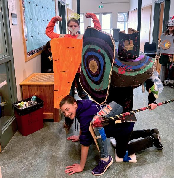 Three elementary school children posing in hallway wearing homemade gladiator costumes painted in bright colours.