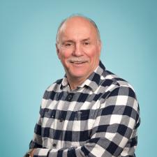 Man with moustache in black and white plaid shirt against teal background.