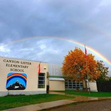 Elementary school with rainbow sign and double rainbow against billowy cloud-covered sky in background