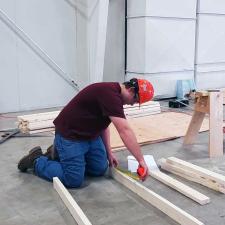 Young man measuring a two by four on a concrete floor