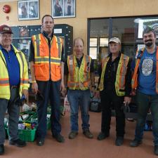 Five people in reflective vests stand in front of an indoor wall