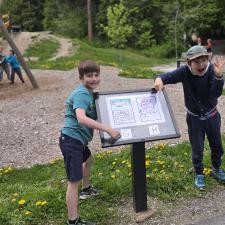 Two grade 3 boys show off a display board at a park where their writing is featured.