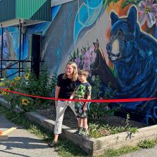 A grade 2 boy helps a female principal cut a ribbon in front of an elementary school