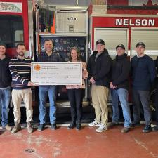 A group of people stand in front of a fire truck holding a large, cardboard cheque