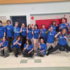 High school students in blue t-shirts pose in a gym while holding up medals hung around their necks.
